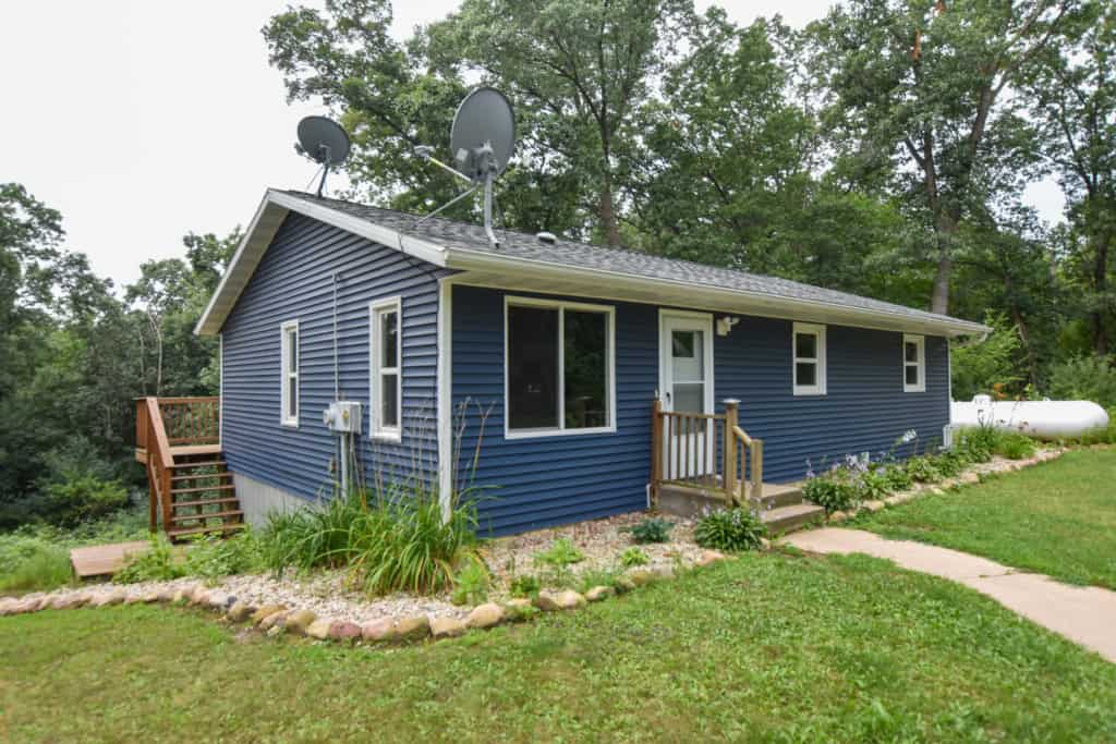 Blue house with a small front porch and back deck in a green yard in Central Wisconsin